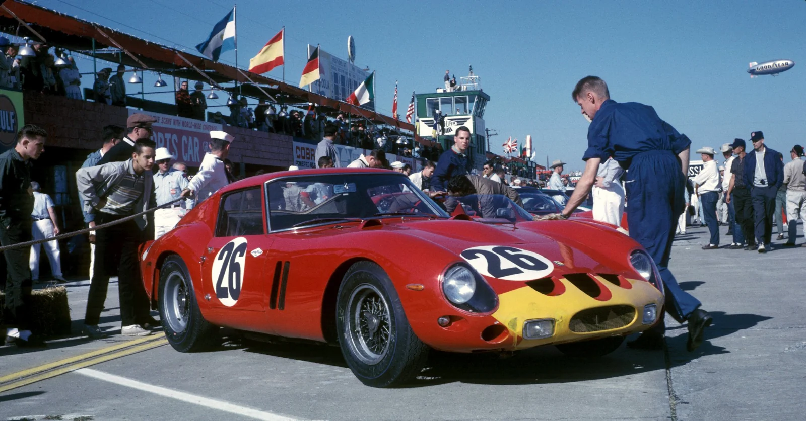 A red racing car surrounded by its crew in an archival paddock photograph.
