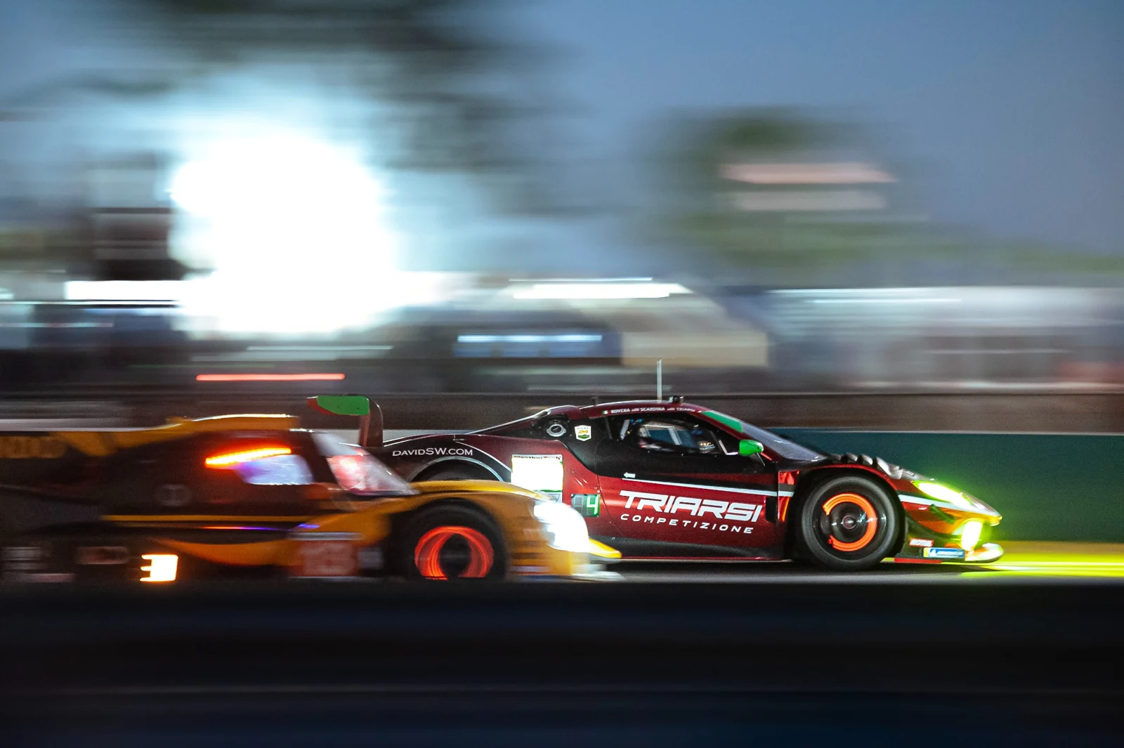 Two race cars passing at night with glowing brake discs.