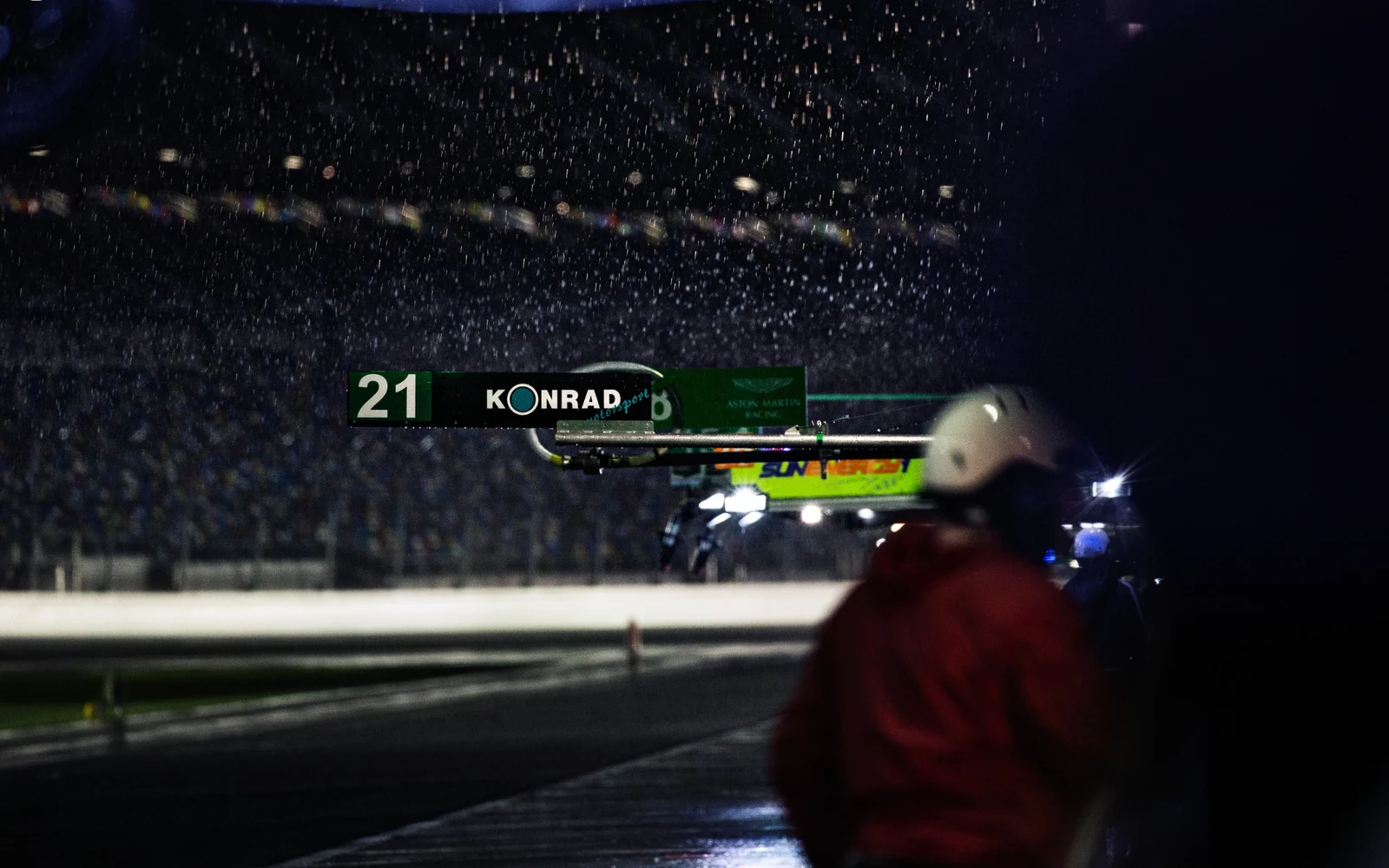 A rear wing and rain in a dark pit lane.