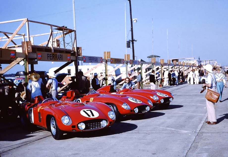 A line of red open-cockpit racing cars outside the garages.