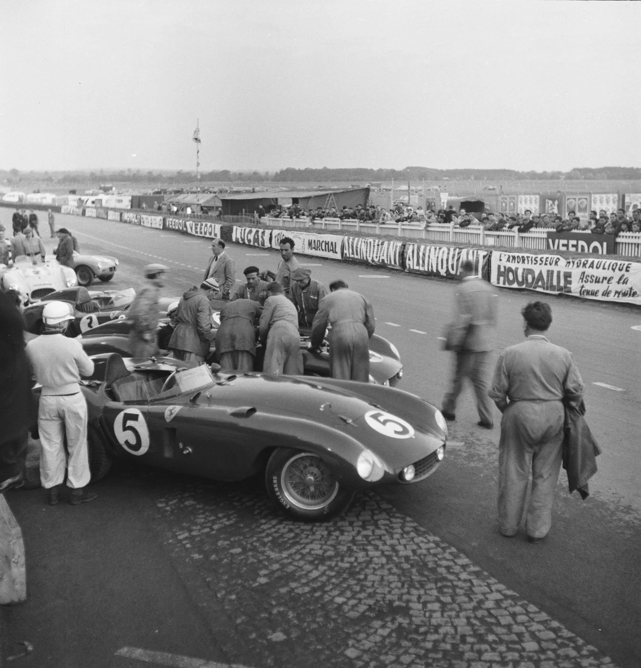 People and racing cars gathering in an archival pit lane.