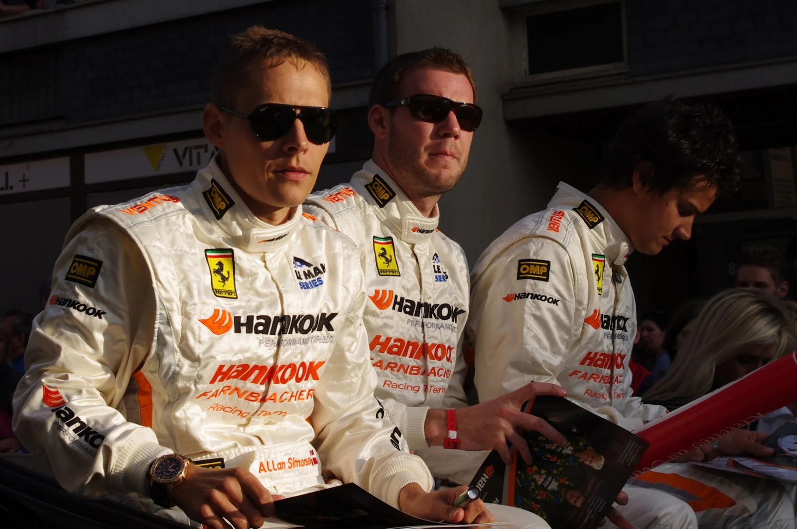 Racing drivers seated at a paddock signing table.